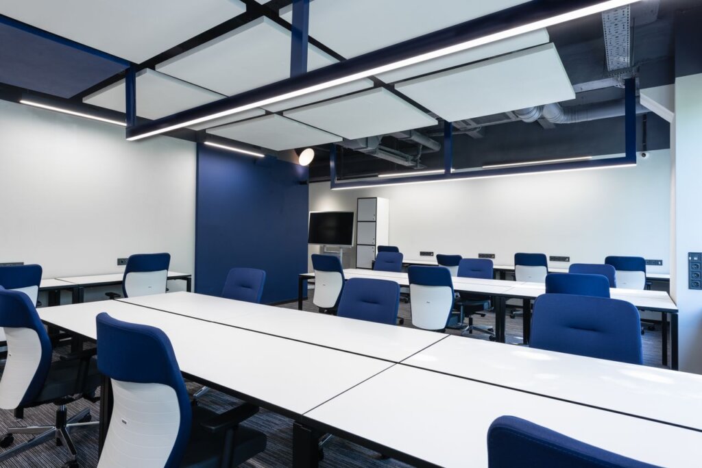 Interior of modern spacious workspace with long white tables and blue armchairs placed near monitor with black screen in business center